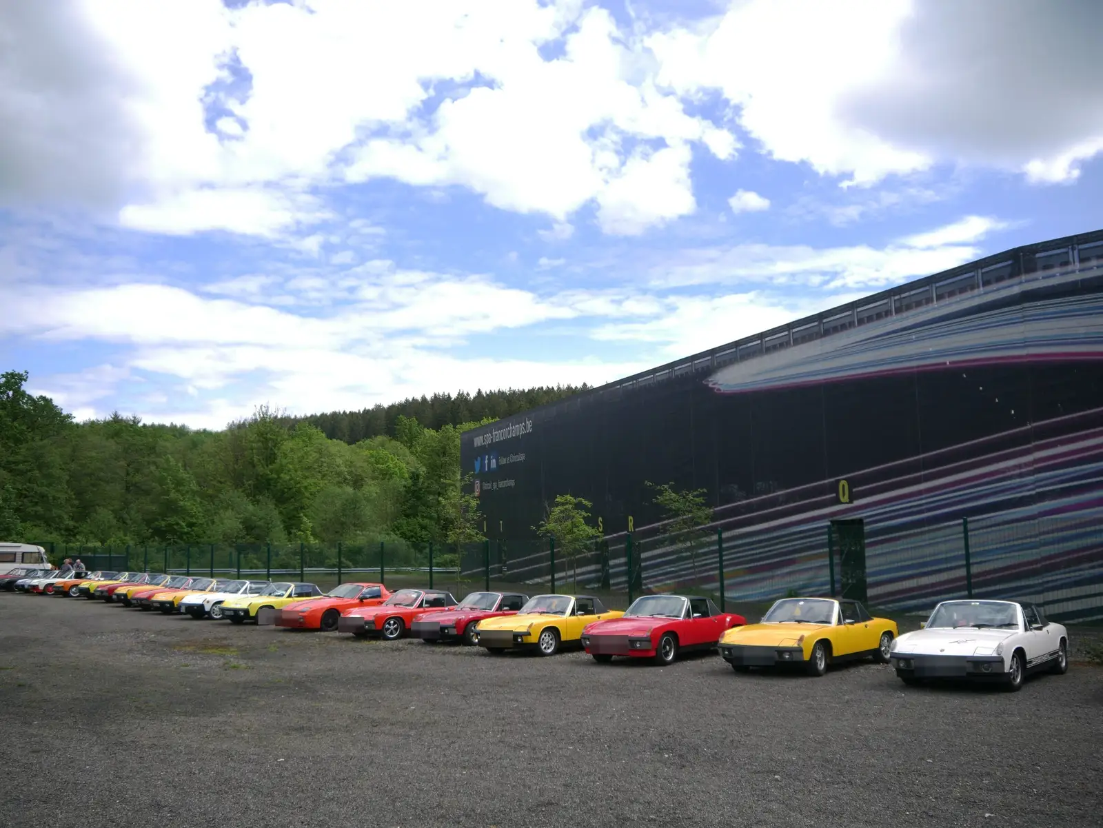 A long line of Porsche 914s in many colours in front of the Spa-Francorchamps circuit.